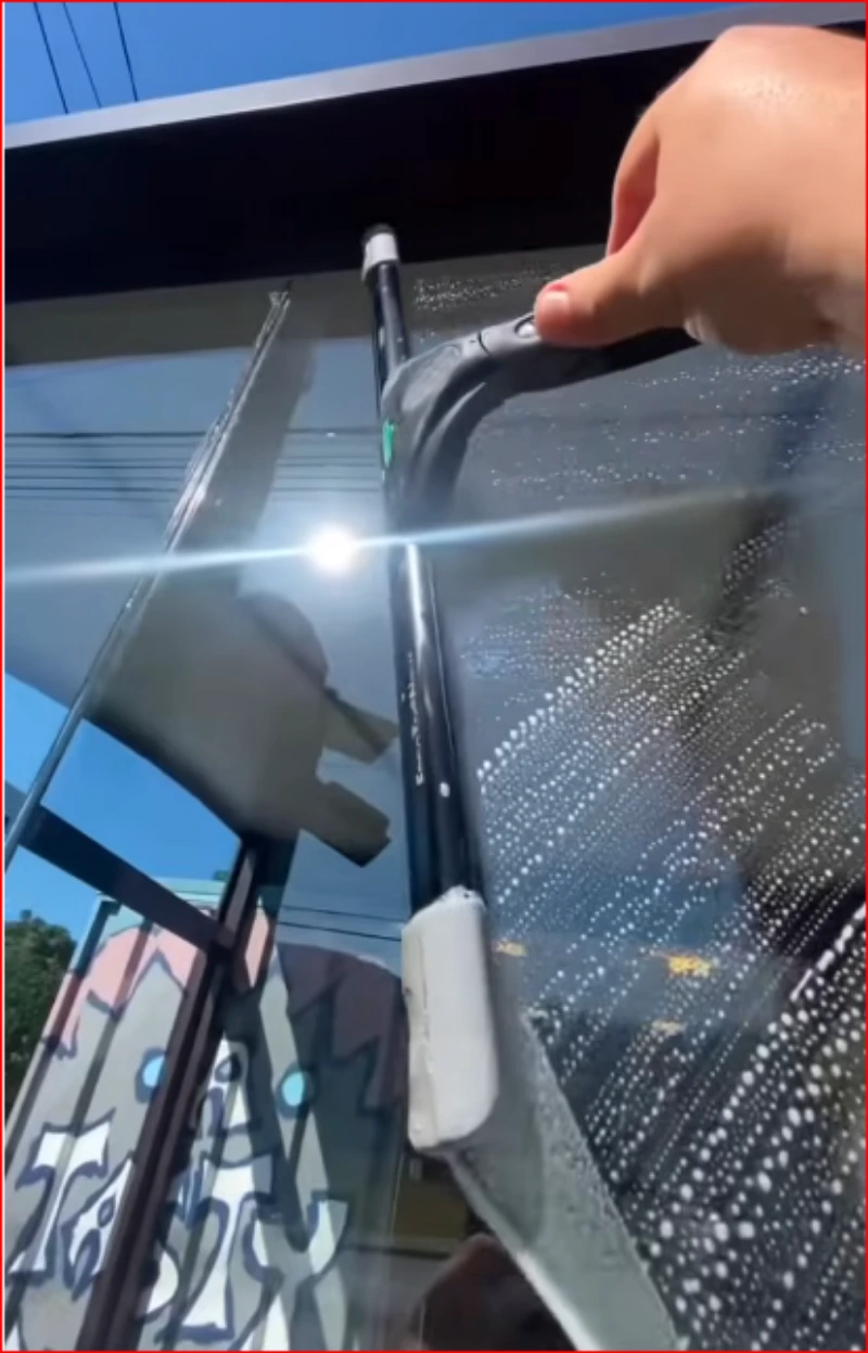 Squeegee pulling soapy water off a window pane from top to bottom, the streak-free method