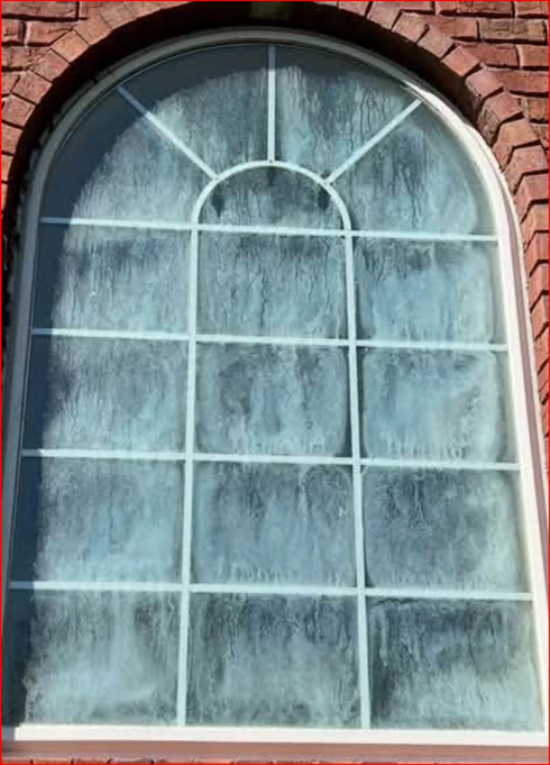 Arched window covered in white mineral spots from sprinkler spray